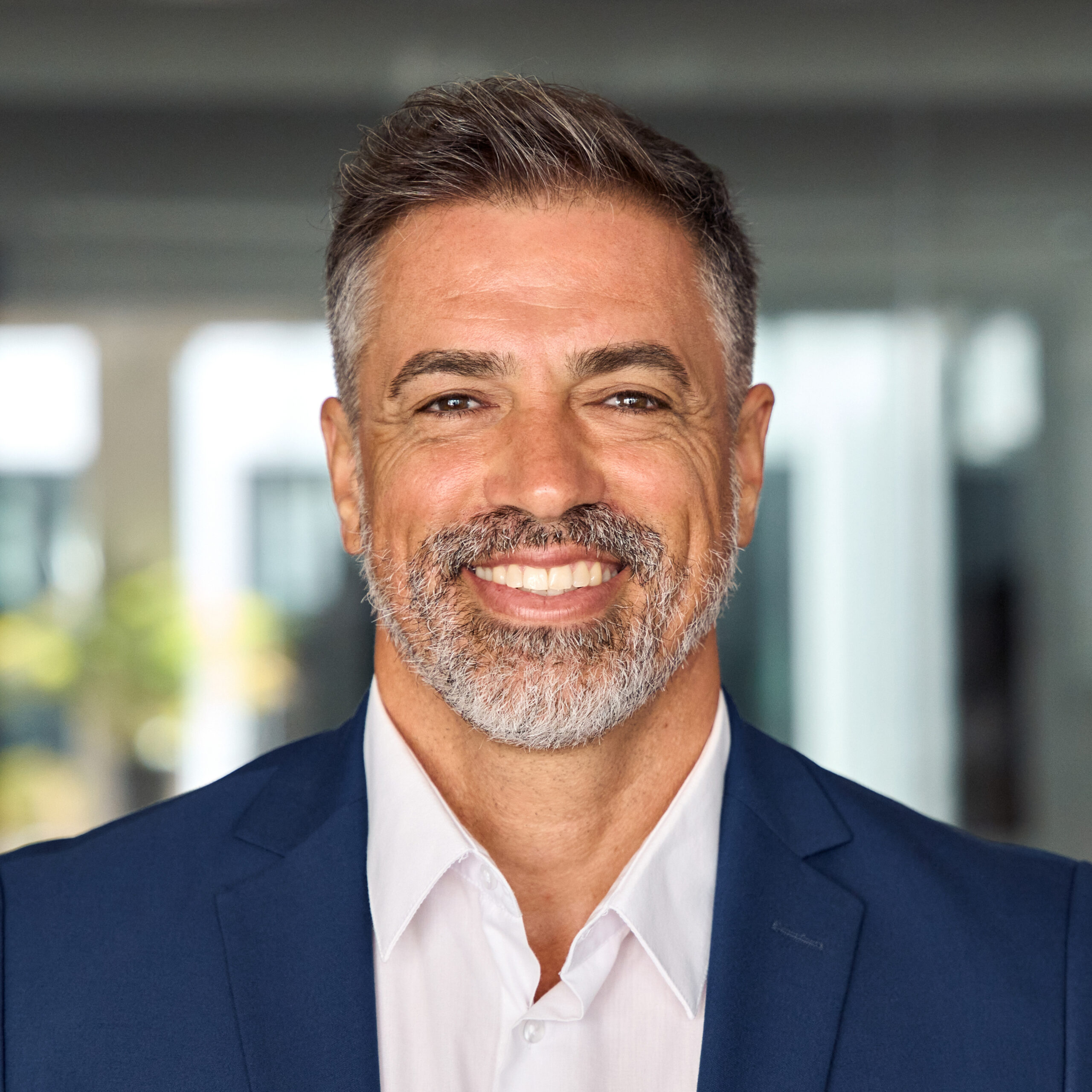 Headshot close up portrait of indian or latin confident mature good looking middle age leader, ceo male businessman in suit on office background. Handsome hispanic senior business man smile at camera.